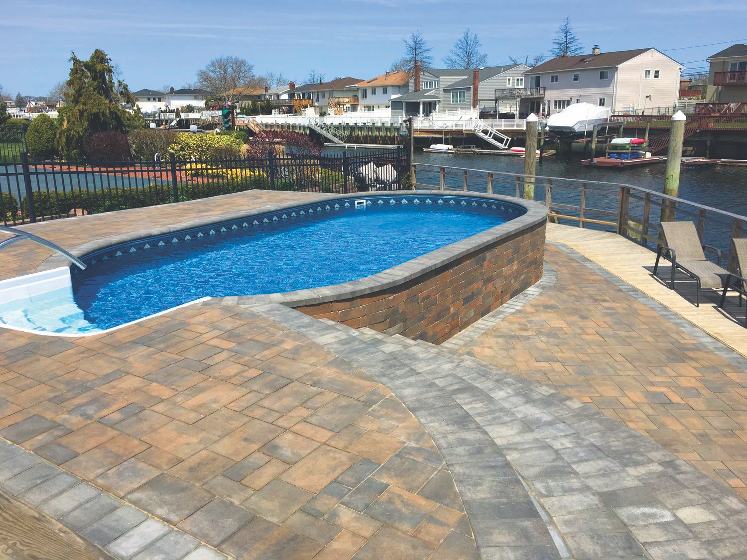 Metric Oval pool semi-inground on canal-side lot with paver deck