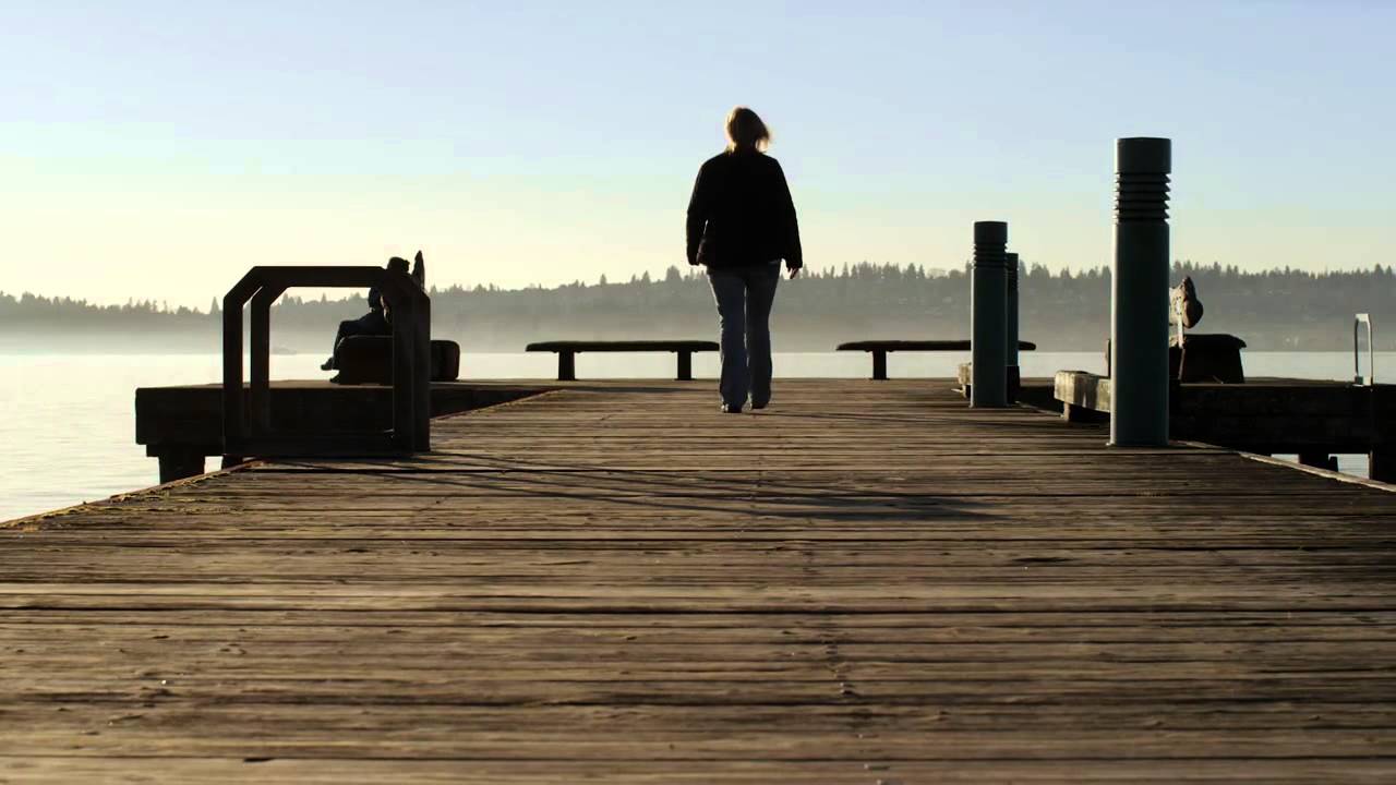 A person seen from behind on a wooden dock overlooking calm water.