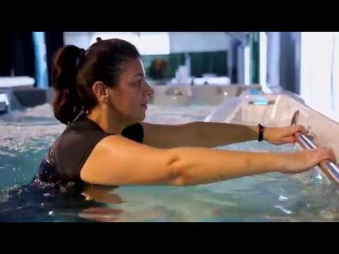 A person in an indoor pool holds a metal rail with both hands.